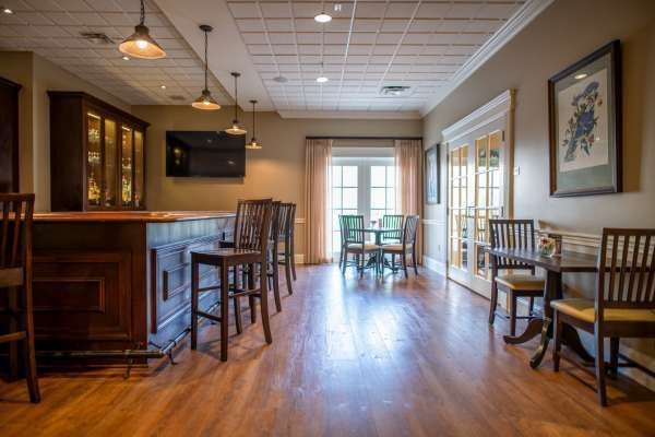 Bar area with wooden bar, stools, and tables. French doors lead to outdoor seating.