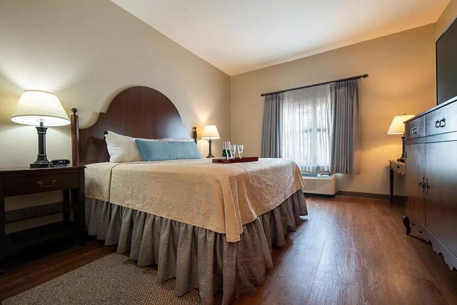 Cozy hotel bedroom with a queen bed, lamps, and wooden furniture.