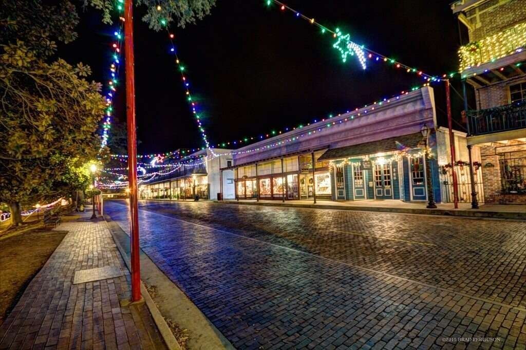Street at night, decorated with colorful lights, illuminated buildings, and cobblestone road.
