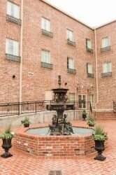 Courtyard with brick fountain, surrounded by a brick building with windows and potted plants.