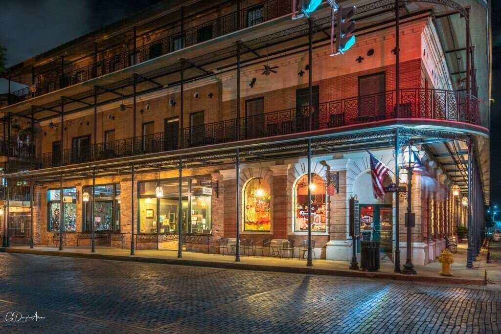 Historic building with illuminated storefronts at night, cobblestone street. American flag.