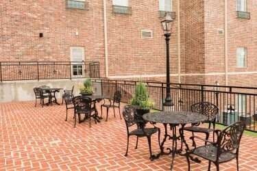 Outdoor patio with brick pavers, wrought-iron tables and chairs, and a brick building.