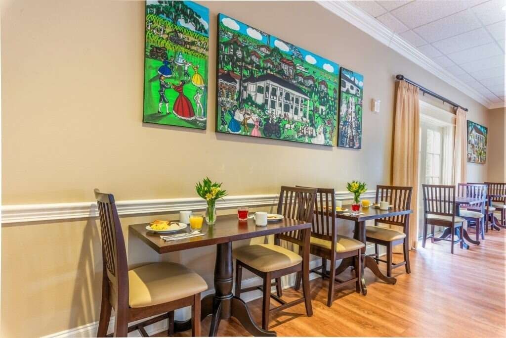 A dining area with tables, chairs, and artwork on the wall. Breakfast is set on the tables.