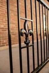 Black iron railing with a fleur-de-lis accent, set against a brick wall.