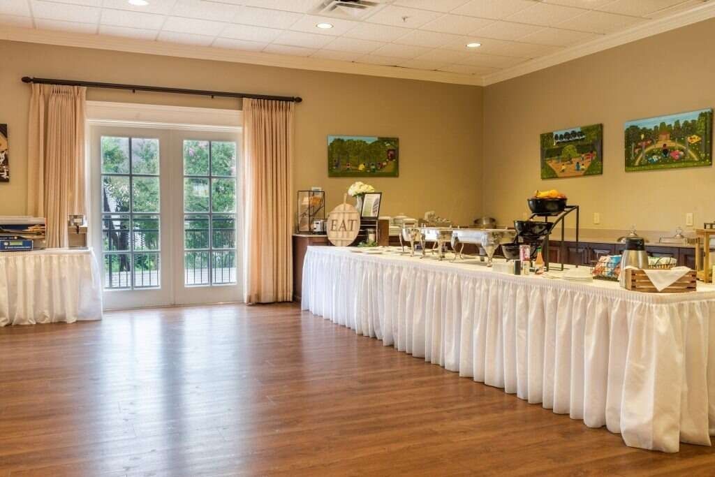 Buffet setup in a banquet hall with a long table covered in white linens. French doors on the left.