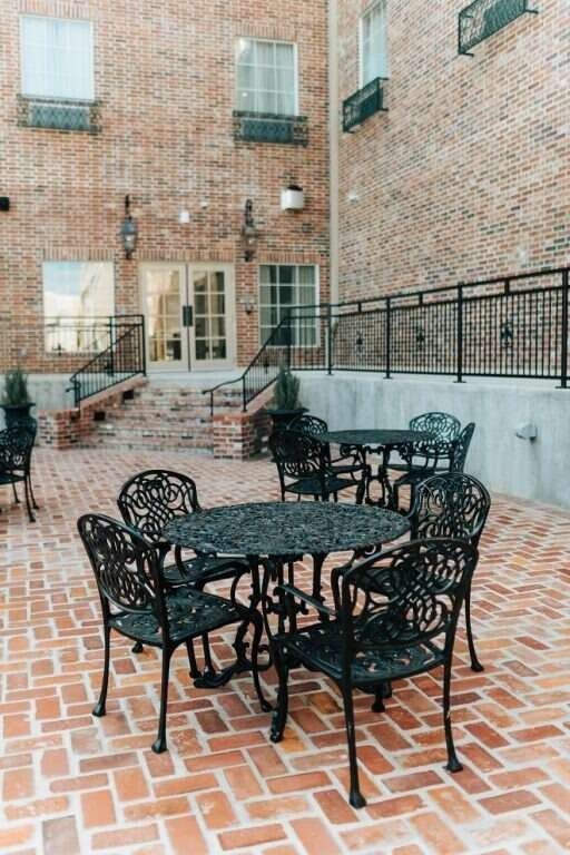 Courtyard with brick paving, black cast iron tables and chairs, and brick building exterior.