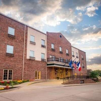Brick hotel with flags, featuring a ramp entrance and windowed floors under a cloudy sky.