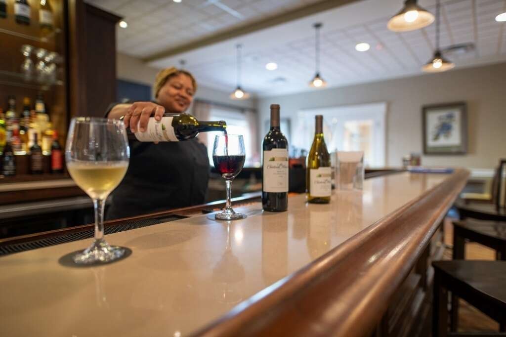 Bartender pouring red wine, with other wine bottles and glasses on the bar in a restaurant.