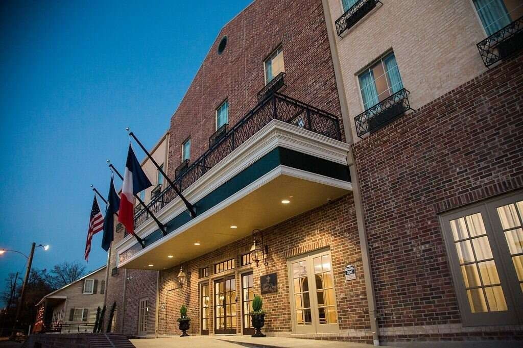 Exterior view of a brick building with a covered entrance, flags, and evening lighting.
