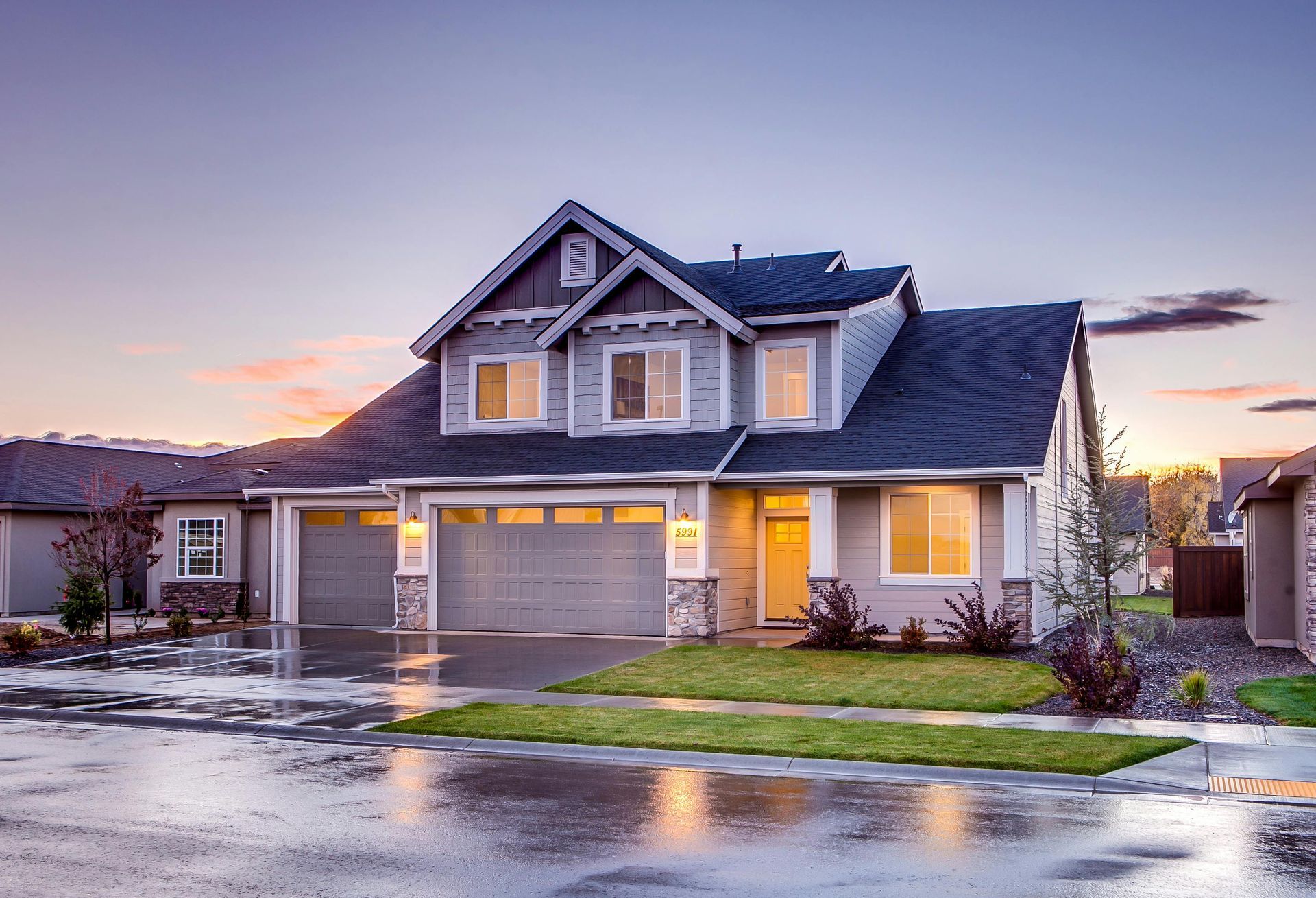 Two-story house with gray siding and roof, wet street, dusk sky.
